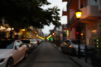 Photo of Blurred view of city street with parked cars in evening