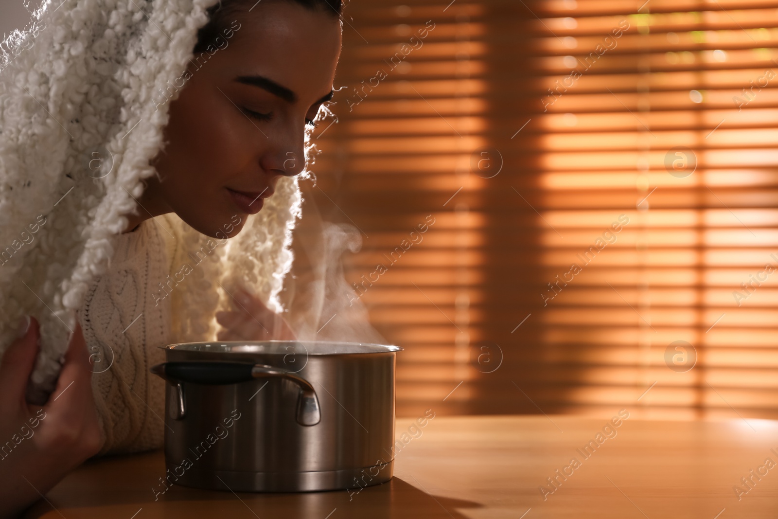 Photo of Woman with plaid doing inhalation above saucepot at table indoors. Space for text