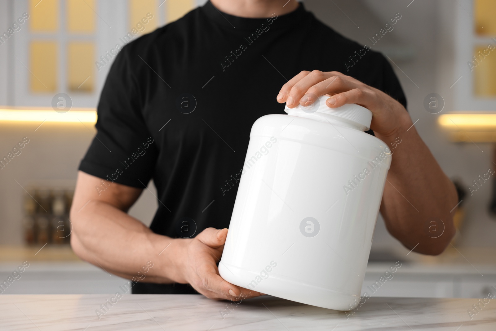 Photo of Young man with jar of protein powder at white marble table in kitchen, closeup