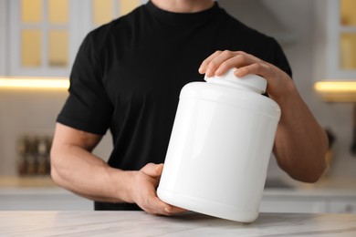 Photo of Young man with jar of protein powder at white marble table in kitchen, closeup