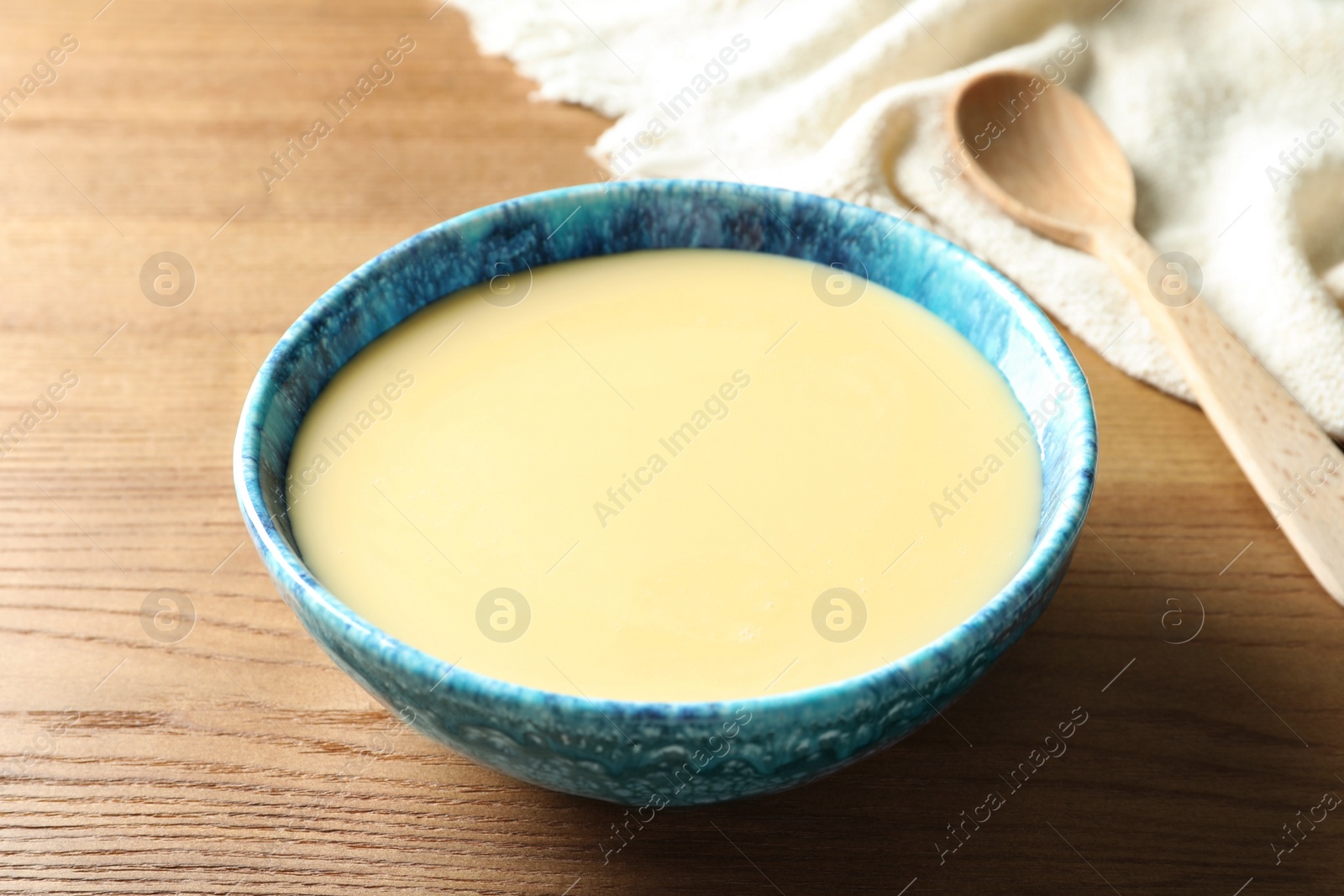 Photo of Bowl with condensed milk on wooden table. Dairy products