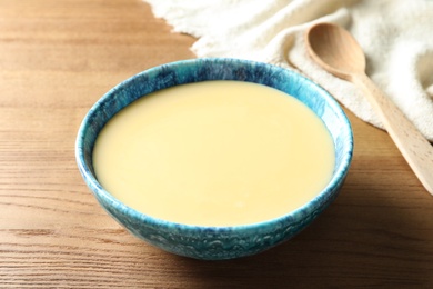 Photo of Bowl with condensed milk on wooden table. Dairy products