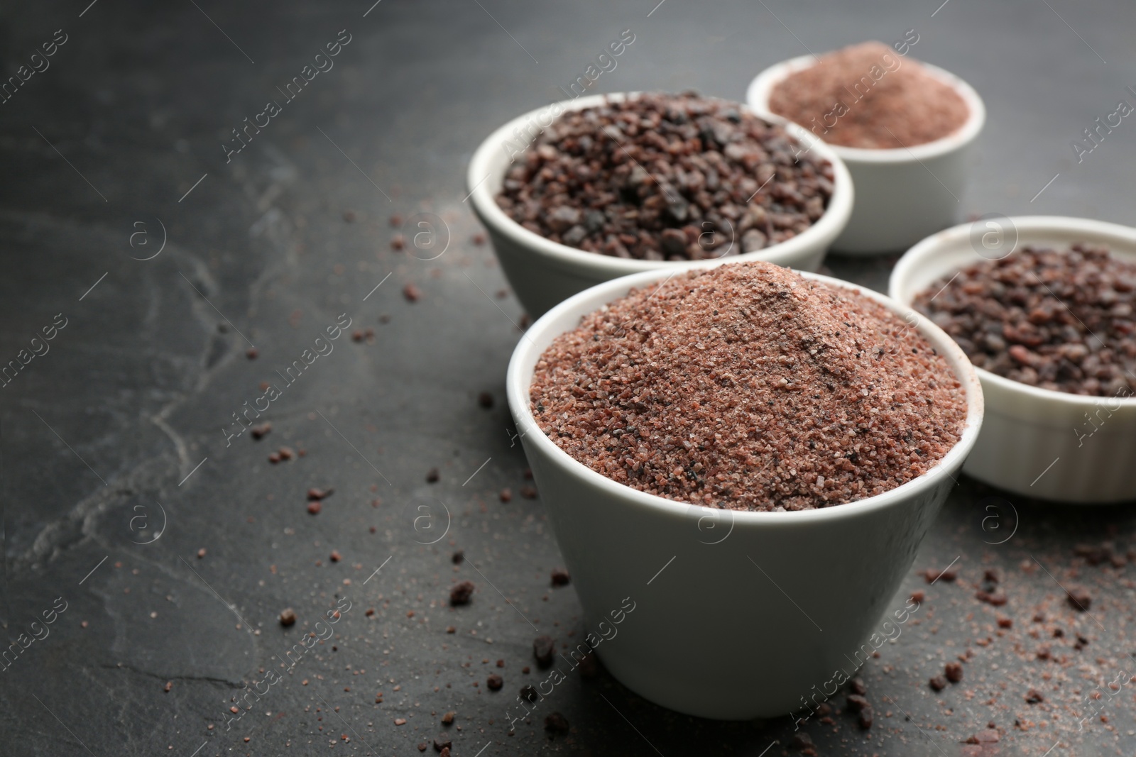 Photo of Ground black salt in bowl on dark slate table. Space for text