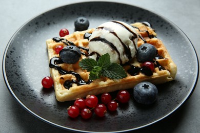 Delicious Belgian waffle with ice cream, berries and chocolate sauce on grey table, closeup