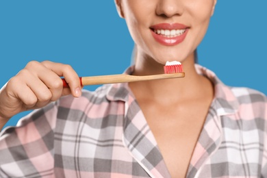 Photo of Woman holding toothbrush with paste on blue background, closeup