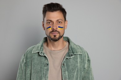 Photo of Man with drawings of Ukrainian flag on face against light grey background