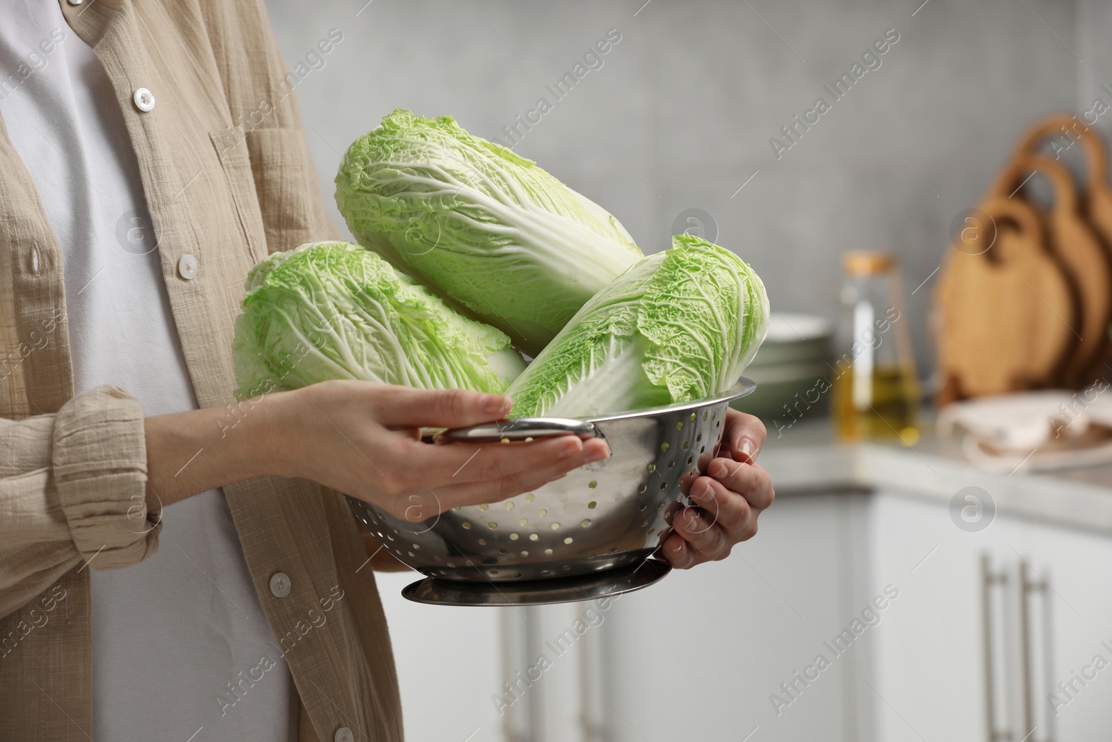 Photo of Woman holding fresh chinese cabbages in kitchen, closeup. Space for text