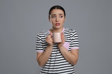 Young woman with cup of hot drink suffering from cold on grey background
