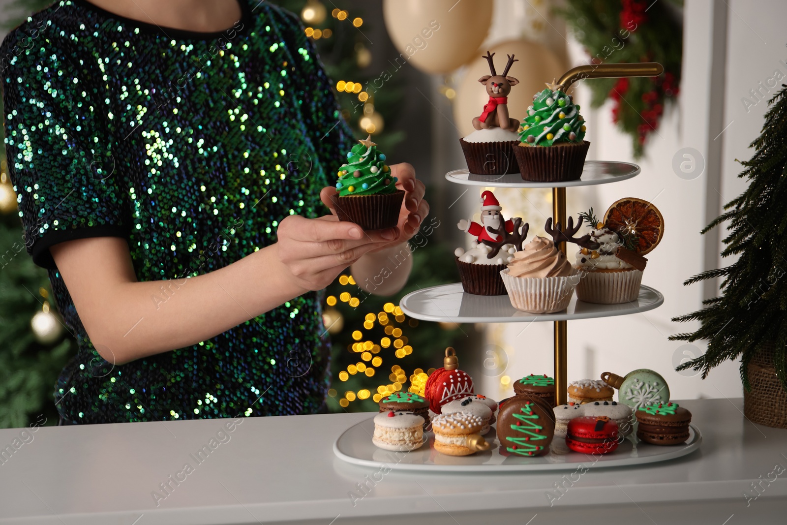 Photo of Woman with Christmas tree shaped cupcake near white table indoors, closeup