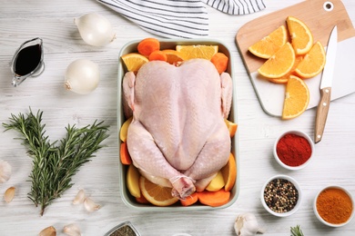 Raw chicken, orange slices and other ingredients on white wooden table, flat lay