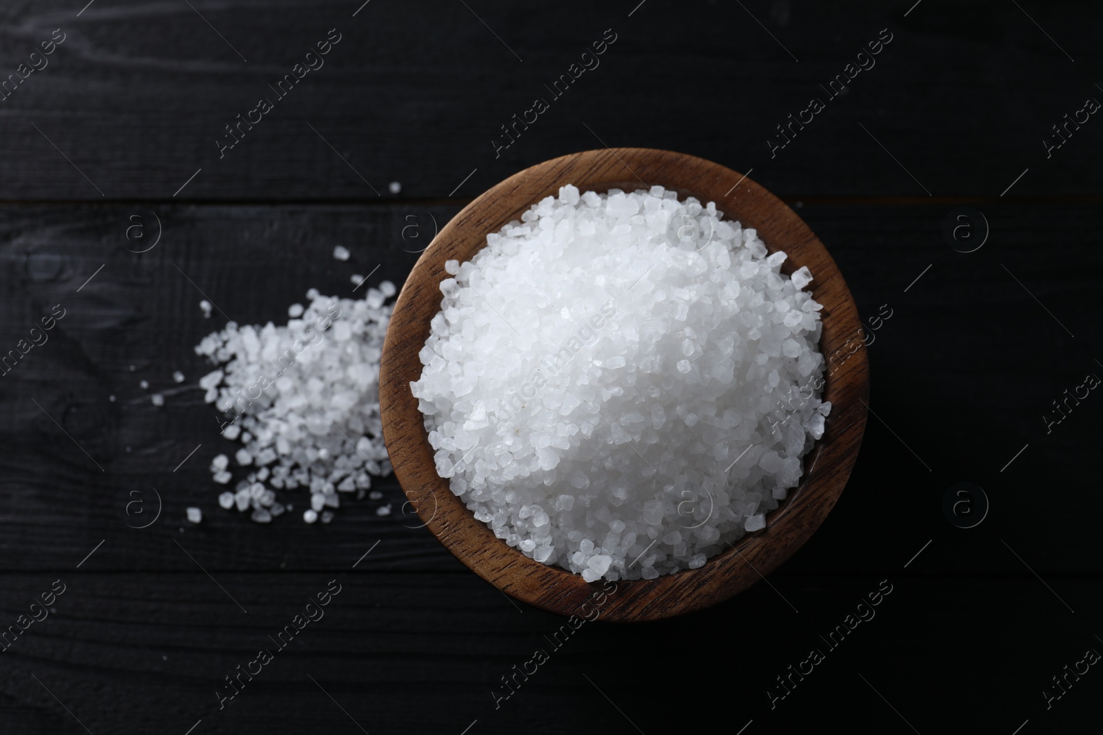 Photo of Organic salt in bowl on black wooden table, top view