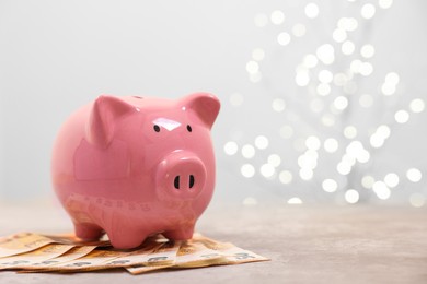 Photo of Piggy bank with euro banknotes on grey table against blurred lights, space for text