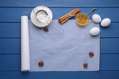 Photo of White baking parchment paper and ingredients on blue wooden table, flat lay