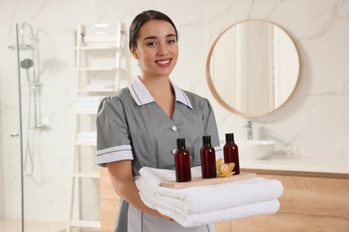 Photo of Chambermaid holding fresh towels with flower and shampoo bottles in hotel bathroom