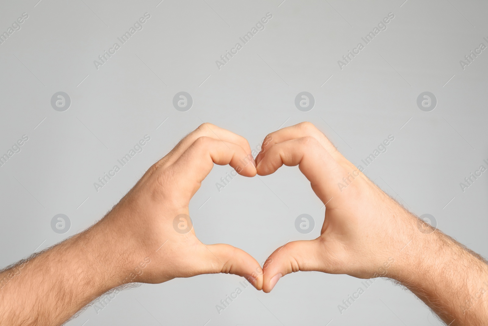 Photo of Man making heart with his hands on light background, closeup