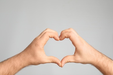 Photo of Man making heart with his hands on light background, closeup