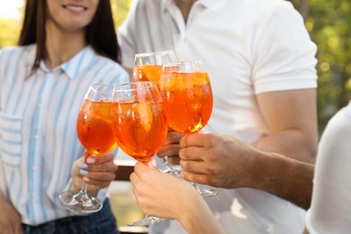 Friends clinking glasses of Aperol spritz cocktails outdoors, closeup