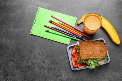 Flat lay composition with tasty sandwich, glass of juice and stationery on grey background