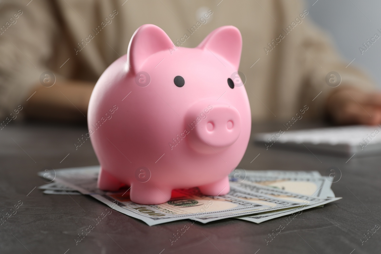 Photo of Woman at black table, focus on pink piggy bank and banknotes