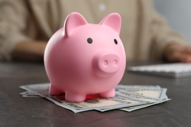 Woman at black table, focus on pink piggy bank and banknotes