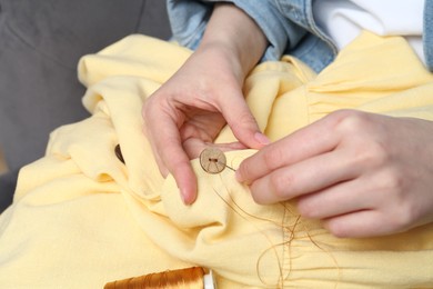 Photo of Woman sewing button with needle and thread onto shirt at home, closeup