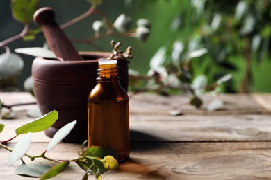 Photo of Bottle of eucalyptus essential oil and plant branches on wooden table, space for text