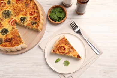 Delicious homemade vegetable quiche, basil leaves and fork on white wooden table, flat lay