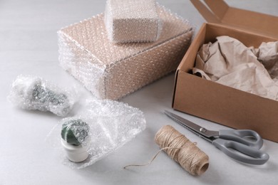 Photo of Fragile ceramic decor elements in bubble wrap near cardboard boxes, scissors and twine roll on light grey table