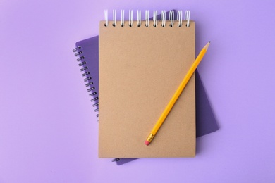 Notebooks with pencil on lilac background, top view