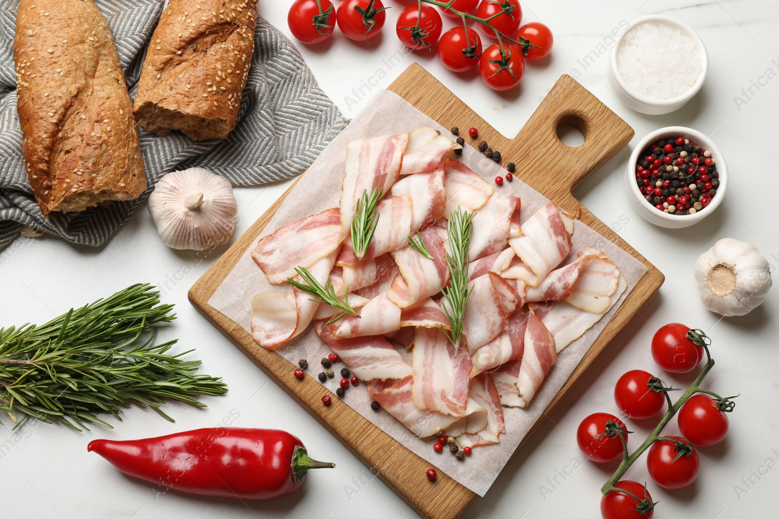 Photo of Slices of raw bacon and fresh products on white marble table, flat lay