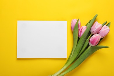 Pink tulips and blank card on yellow background, flat lay. Space for text