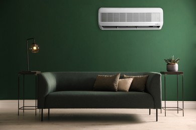 Image of Modern air conditioner on green wall in room with stylish sofa