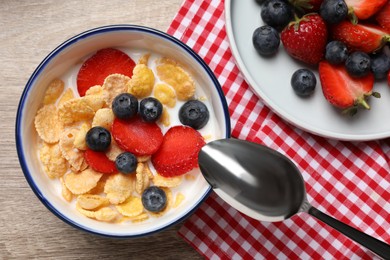 Photo of Delicious crispy cornflakes with milk and fresh berries on wooden table, flat lay