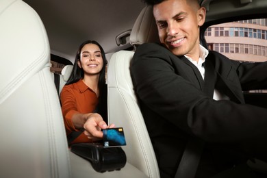 Photo of Young woman paying for service using credit card via payment terminal in modern taxi