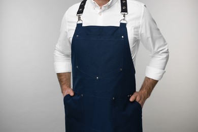 Man wearing kitchen apron on grey background, closeup. Mockup for design