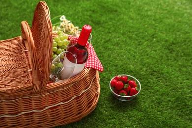Photo of Picnic basket with wine and fruits on grass. Space for text
