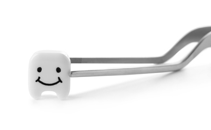 Dental tweezers and small plastic tooth with cute face on white background