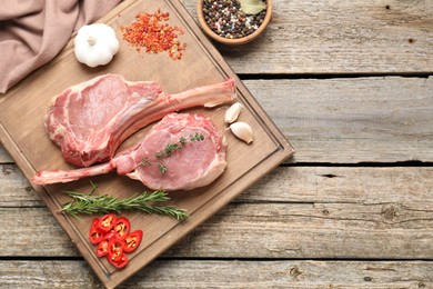 Photo of Fresh tomahawk beef cuts and spices on wooden table, top view. Space for text