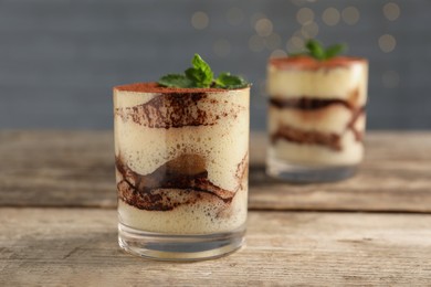 Photo of Tasty tiramisu and mint in glasses on wooden table, closeup