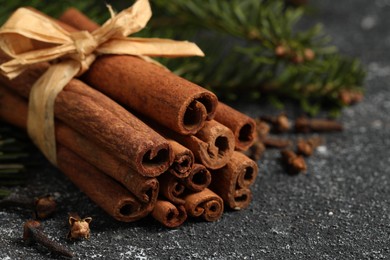 Photo of Different spices. Aromatic cinnamon sticks and clove seeds on dark gray textured table, closeup