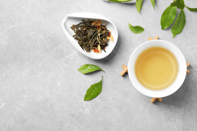 Photo of Cup of green tea, dry and fresh leaves on grey table, flat lay. Space for text