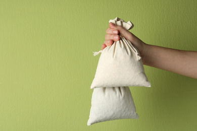 Photo of Woman holding full cotton eco bags on light green background, closeup. Space for text
