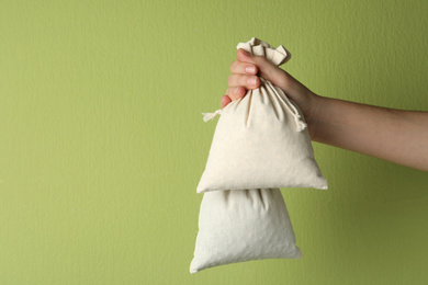 Woman holding full cotton eco bags on light green background, closeup. Space for text