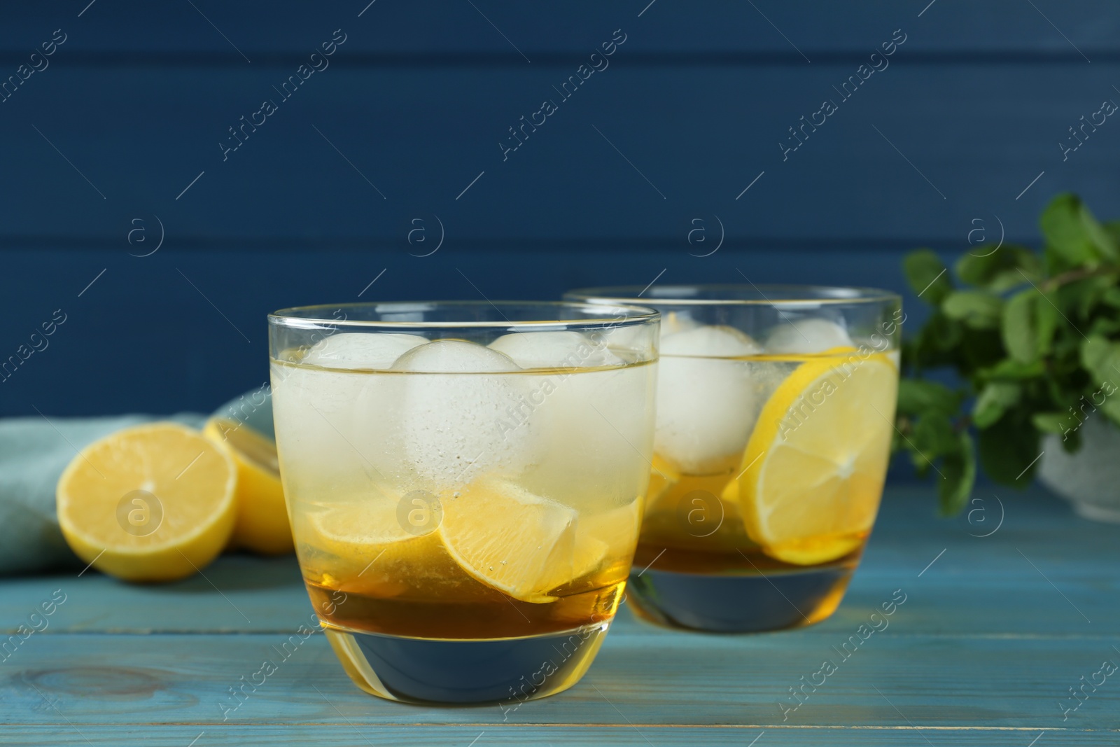 Photo of Delicious cocktails with lemon and ice balls on light blue wooden table