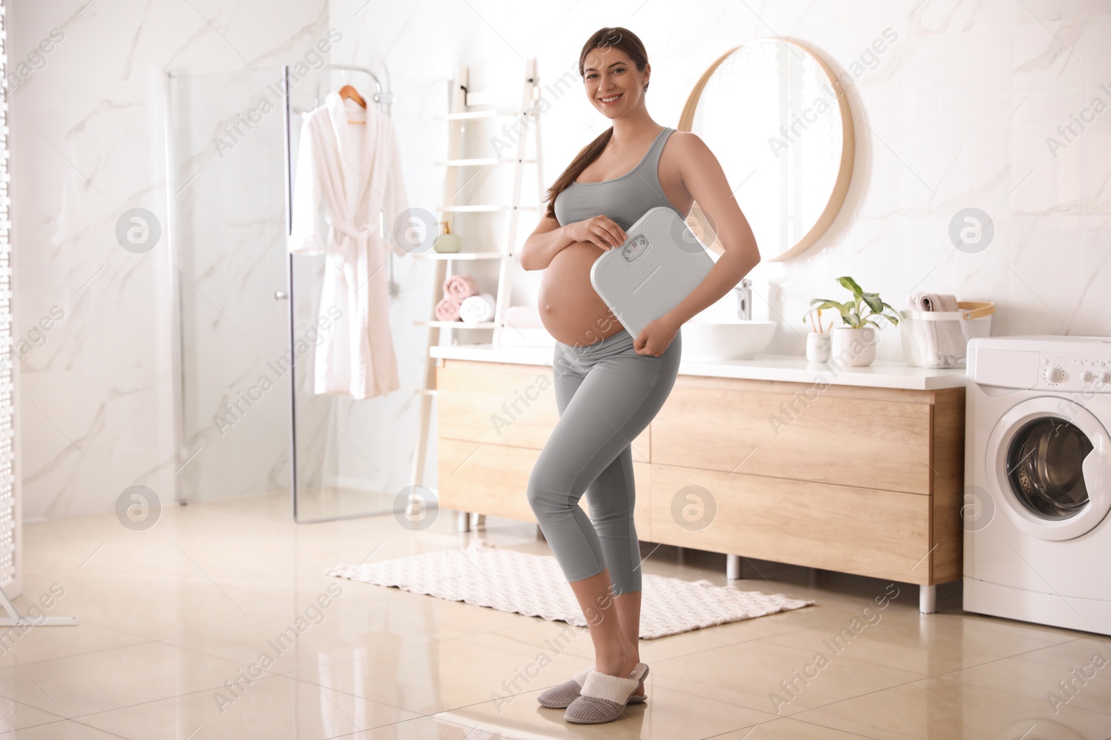 Photo of Young pregnant woman with scales in bathroom