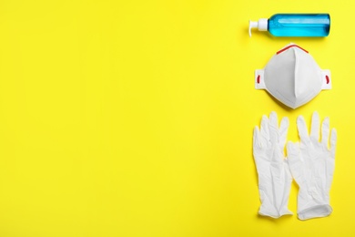 Photo of Medical gloves, respiratory mask and hand sanitizer on yellow background, flat lay. Space for text