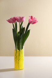 Photo of Yellow filler with tulips in glass vase on white table. Water beads