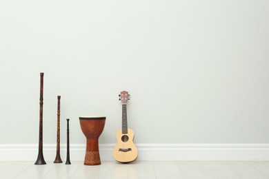 Photo of Ukulele, vintage bryolkas and hand drum near white wall indoors, space for text. Musical instruments