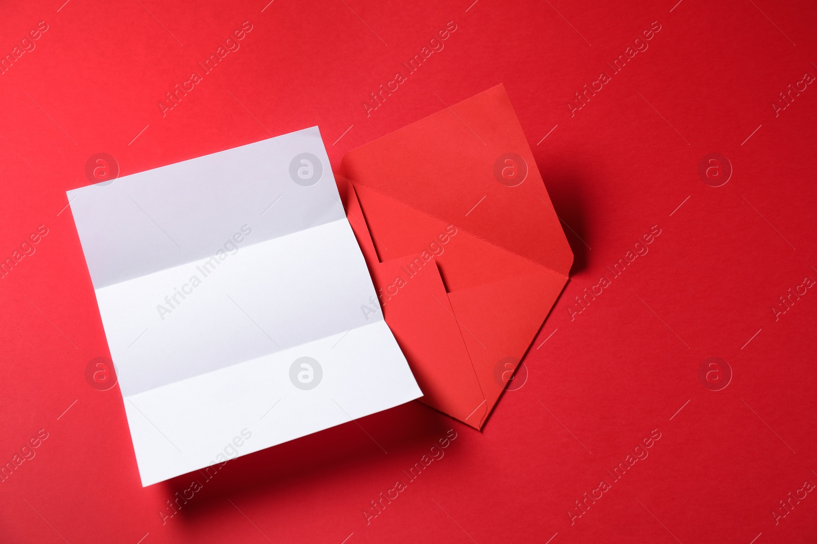 Photo of Blank sheet of paper and letter envelope on red background, top view. Space for text