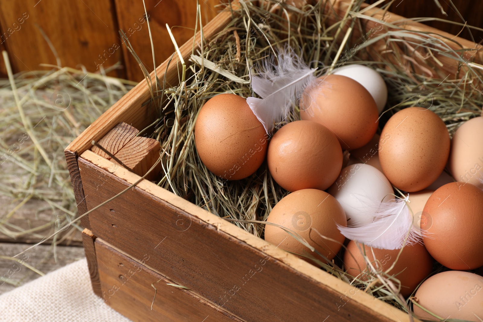 Photo of Fresh chicken eggs and dried hay in wooden crate on table, closeup